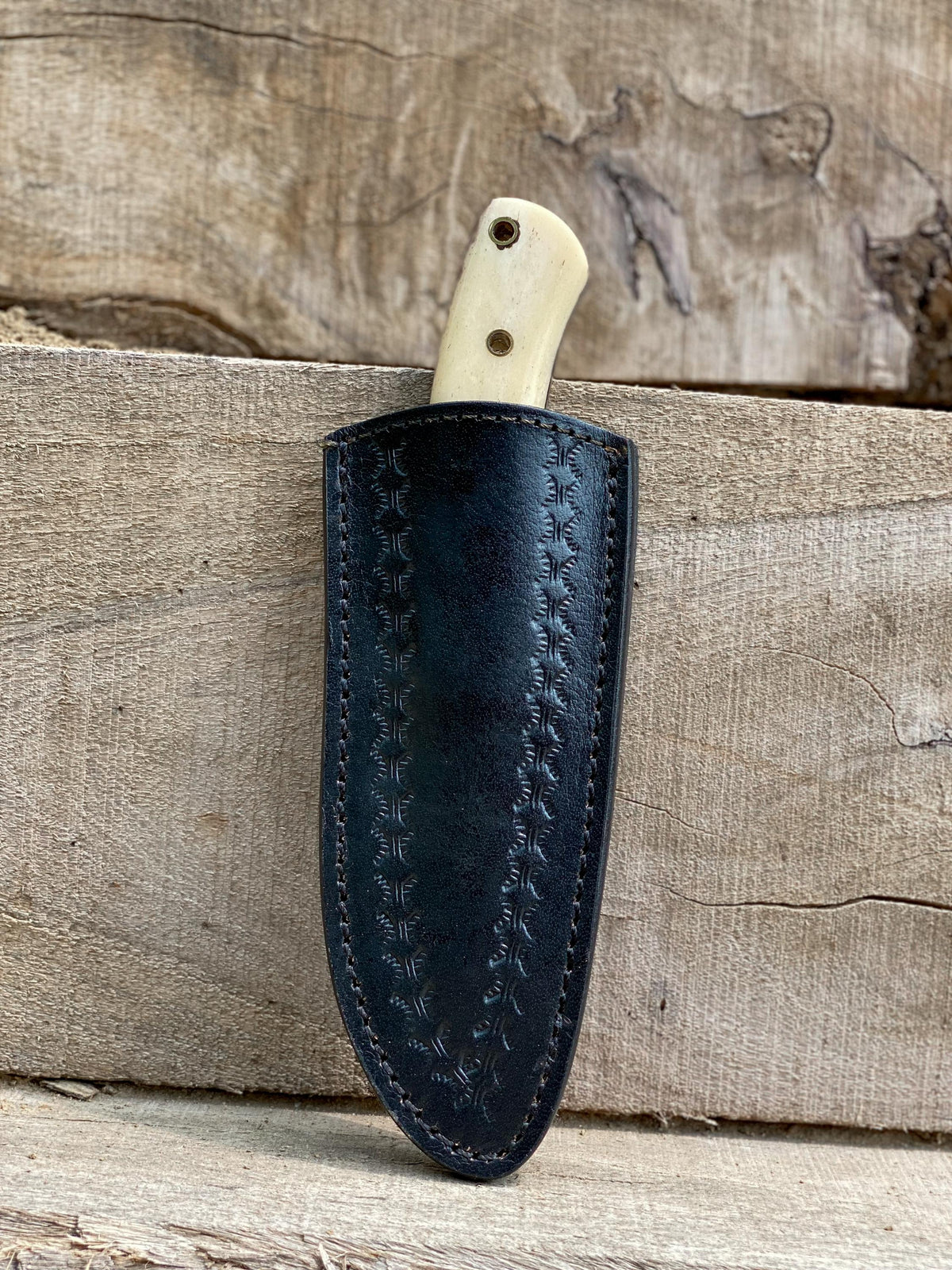 Black leather knife sheath with a white handle on a wooden background